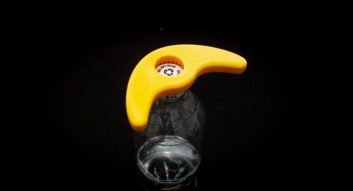 Yellow boomerang shaped bottle opener with circular opening attached to bottle cap of water bottle