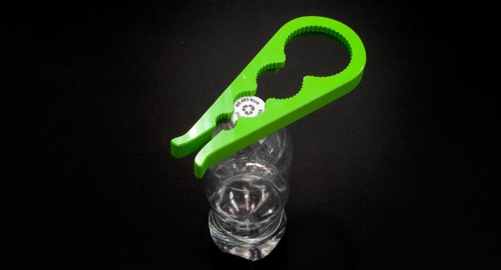 Green bottle opener with four differently sized holes for opening is attached to top of bottle.