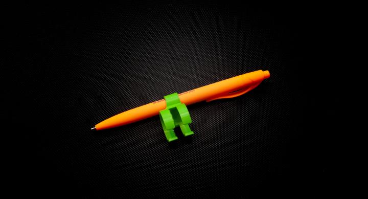 Green finger pencil holder with slot for orange pen to fit through, and a connected opening for a finger